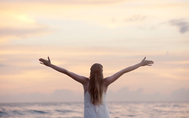夕暮れの海辺で両手を広げる女性